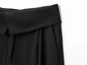 Close-up of black twill trousers showing raw edge details and folded waistband design
