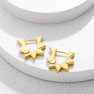 Detail view of 18K gold plated gear shape earrings on white geometric pedestal
