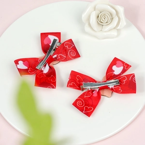 Set of two red ribbon bow hair clips with white heart patterns on a stylish white plate