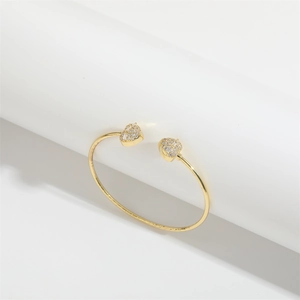 Detailed view of a gold-finish open bracelet featuring two shimmering heart-shaped charms