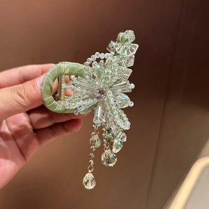 Detailed close-up of a luxury floral hair claw clip with crystal tassels and green fabric