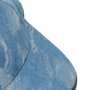Macro shot of blue washed denim baseball cap with white stitching and floral texture