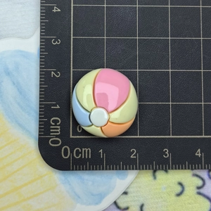 Macro shot of a 2.5cm colorful resin beach ball charm next to a measuring ruler