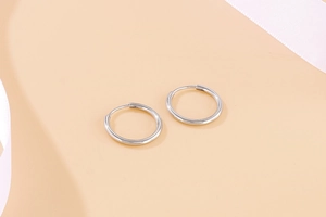 Close-up of polished stainless steel hoop earrings on light beige silk background