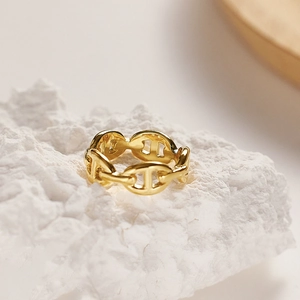 Macro shot of gold pig nose chain link ring on white textured stone surface