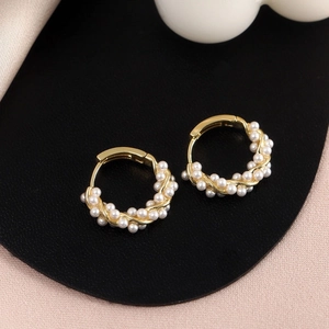 Detailed macro view of twisted gold hoop earrings with small pearls on black stand