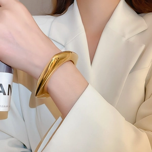 Polished chunky gold wavy bangle on model's wrist with minimalist metal design