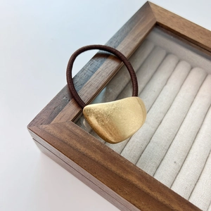 Detailed macro view of an elastic hair tie with a matte gold pebble-shaped metal charm