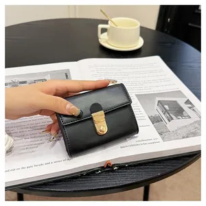 Close-up of black leather card holder with gold metal clasp on a wooden table