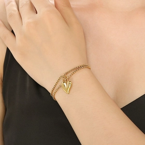 Detail of a double-layered gold bracelet with a heart pendant on a woman's wrist