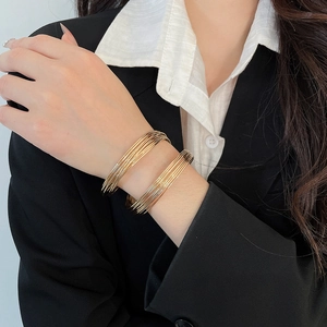 Detail of layered gold twisted cuff bracelet on wrist with elegant business attire