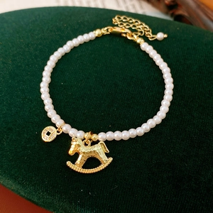 Detail of pearl bracelet with golden horse and coin charms on dark green velvet