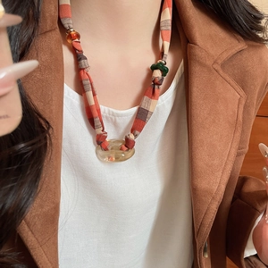 Detail of orange plaid fabric necklace with amber resin rings and dark green beads