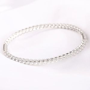Macro detail of silver bead bracelet with diamond-cut texture on white silk background