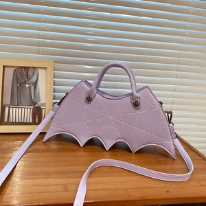 Purple bat-shaped handbag with spider web stitching and silver hardware on a wooden table