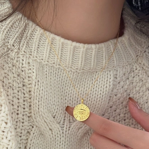 Close-up of a gold 925 silver necklace with a round evil eye coin pendant on a model