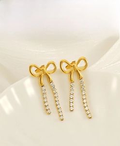 Macro detail of gold stainless steel bow earrings with hanging rhinestone tassels