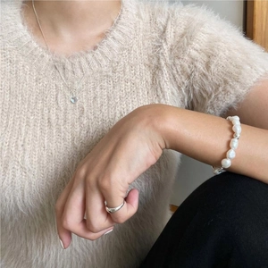 Baroque pearl bracelet with round beads and minimalist ring on a soft knit sweater