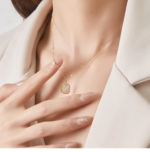 Close-up of golden octagonal necklace with shell inlay worn by model in beige blazer