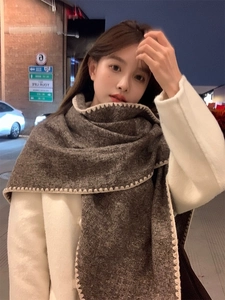 Detail of dark brown knit scarf with contrast cream stitching worn by model