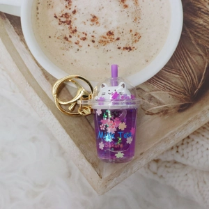 Detail of purple milk tea cup keychain with a cute white cat and floating sakura petals