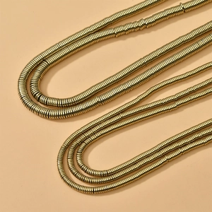 Collar de capas doradas con cuentas de disco de metal sobre un fondo beige suave