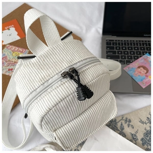 Detailed view of white corduroy mini backpack with black zippers on cozy bed setup