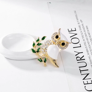 Exquise broche hibou dorée avec émail blanc et cristaux sur une branche à feuilles vertes