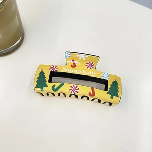 Close-up of yellow Christmas hair claw clip with Santa Baby lettering and holiday motifs