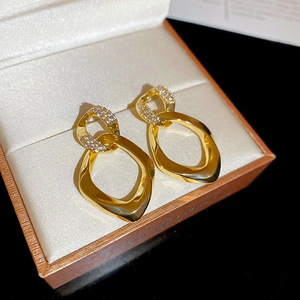Macro shot of twisted gold oval earrings with zircon accents on beige silk display