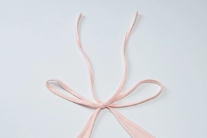 Detailed macro view of a soft pink fabric ribbon tied into a bow on a stylish garment