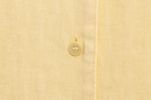 Close-up of high-quality yellow linen fabric texture and resin button on shirt placket