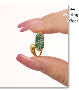 Détail macro d'une bague ouverte dorée ornée de zircons verts sertis et d'un fini poli brillant