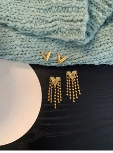 Detailed view of golden V-shaped stud earrings and chain fringe pendants on blue knit