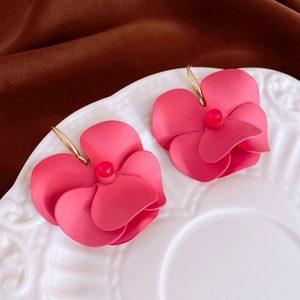 Macro detail of matte pink flower earrings with golden hooks on a textured surface