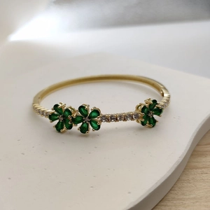 Macro shot of green gemstone clover flower and white zircon pavé on golden bangle