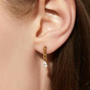 Macro shot of gold Cuban link earrings with a hanging teardrop zircon on a model