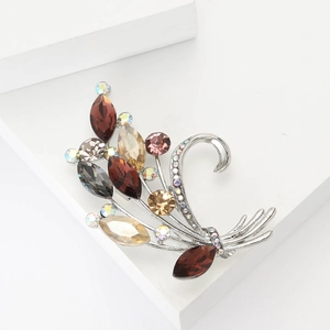 Elegant silver flower bouquet brooch with champagne and brown crystals on a white pedestal