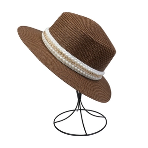 Detailed view of brown woven straw hat featuring white pearls and gold chain trim
