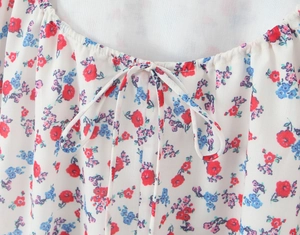 Close-up of neckline with bow tie and red-blue floral embroidery on white fabric