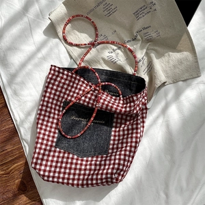 Macro detail of red checkered canvas tote featuring a denim pocket and colorful bead strap