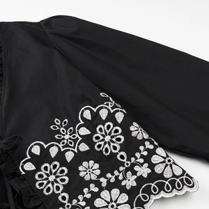 Close-up of black shirt cuff with white eyelet flower embroidery and scalloped edges