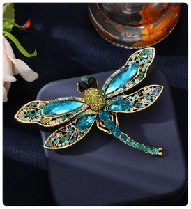 Detailed close-up of a luxury dragonfly brooch with colorful crystals on a navy gift box