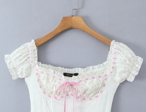 Détail du haut à fleurs blanches avec manches bouffantes et petit nœud rose à carreaux