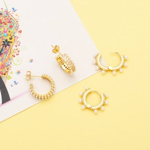 Detail of C-shaped gold hoop earrings with white pearls and sparkling zircons set