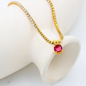 Close-up of golden necklace featuring a large red zircon pendant and micro-pave crystals