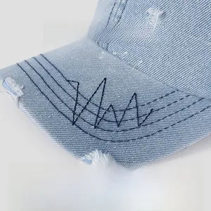 Detail of distressed denim baseball cap showing frayed holes and contrast stitching