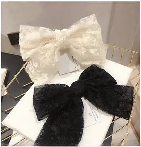 Close-up of large lace bow hair clips in black and cream on a decorative card