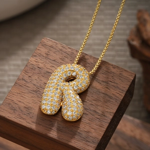 Macro detail of 18K gold plated letter R pendant with sparkling pavé zircons on wood