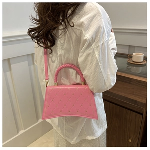 Pink quilted trapezoid handbag with heart patterns and woven handle shown on shoulder
